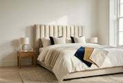 Hand-finished upholstered bed with a channel-tufted linen headboard and a fan of fabric swatches in warm morning light