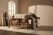 An upholstered bed being hand-finished on a workbench in a Yorkshire workshop, fabric and tools laid out in warm daylight.