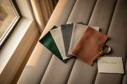 Fan of velvet, chenille, bouclé and linen fabric swatches laid on an upholstered Belsogno headboard in natural light