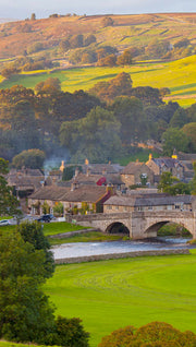 Yorkhire Town with stone bridges over a river, surrounded by green fields and trees.