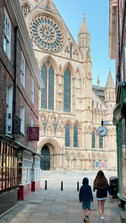 Two people walking towards Yorkshire  cathedral with a prominent rose window.