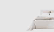 Bed with beige bedding and pillows on a light gray background