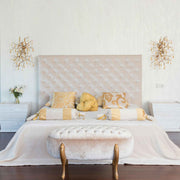 Neatly made bed with decorative pillows and a tufted bench in a bedroom setting.